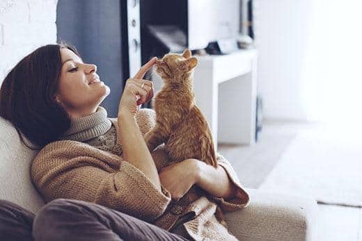 Frau sitzt auf Sofa, hält eine getigerte Katze und streichelt ihre Nase